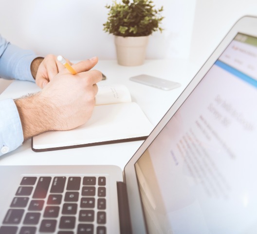 Laptop And Hand of Man Writing Notes