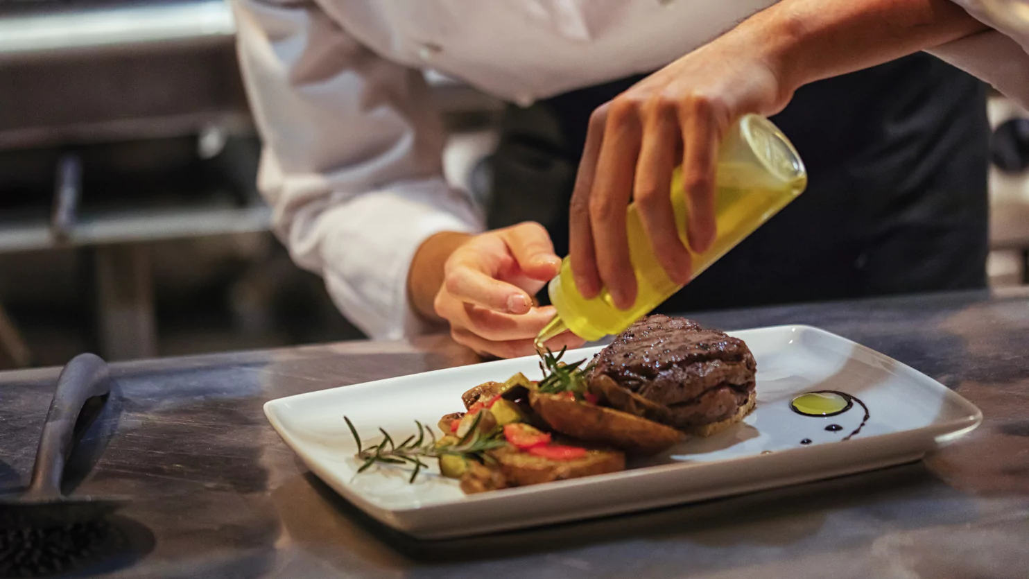 A chef pouring oil on a plate of meat.