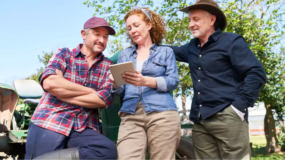 Three people standing in front of a tractor examining a tablet.