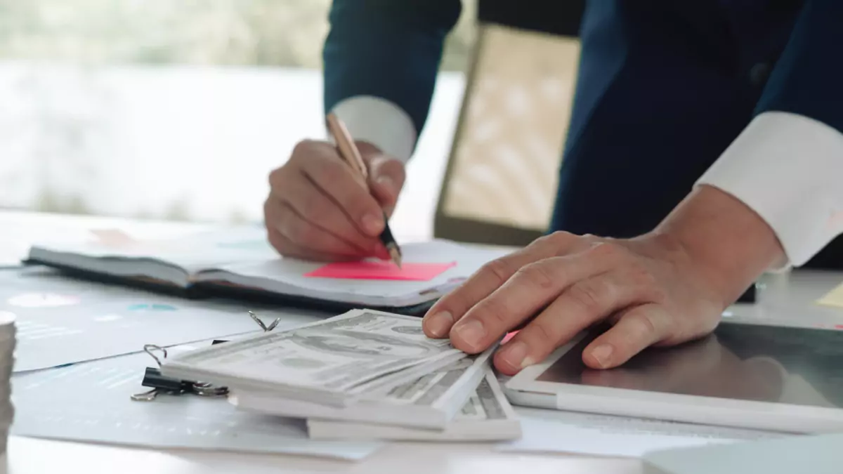 Man Writing on Paper and Touching Dollar Paper Bill