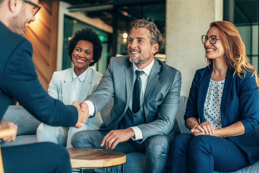 A group of professionals in suits smiling during a handshake agreement inside a modern office lounge.