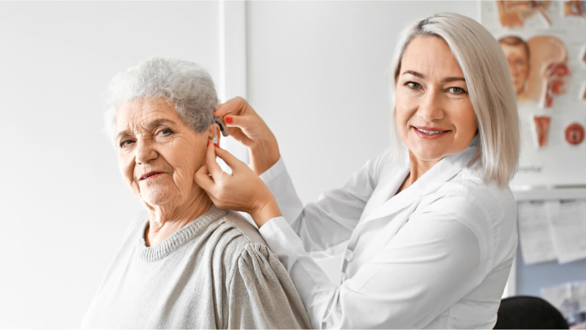 Woman putting hearing aid to an older woman