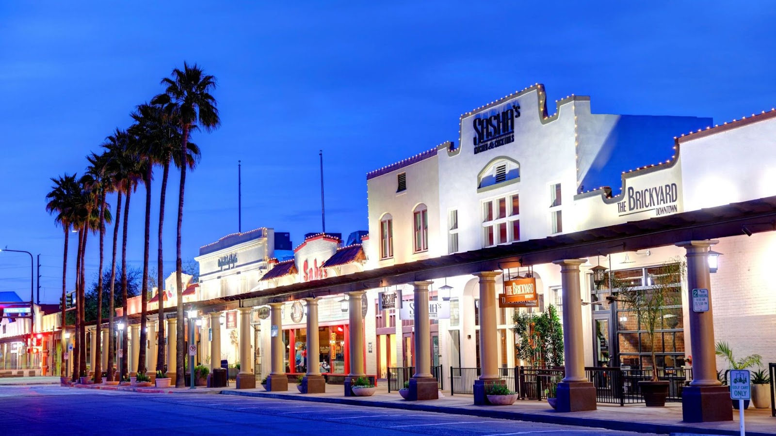 A row of palm trees line a street in front of a building