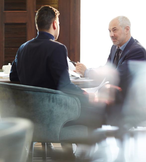 A senior professional holding a pen while discussing financial documents across a table with a colleague.