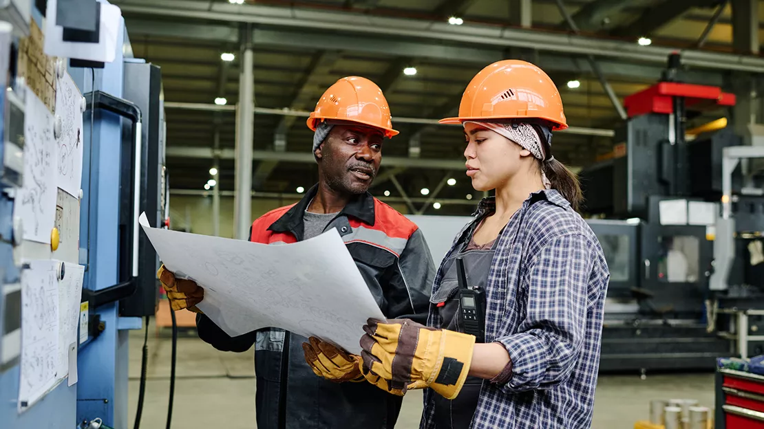 Two people wearing hardhats looking at a blueprint