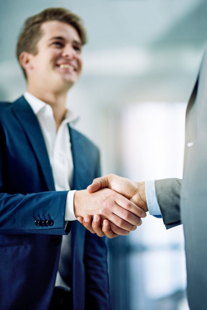 A young man in a suit shaking another person's hand