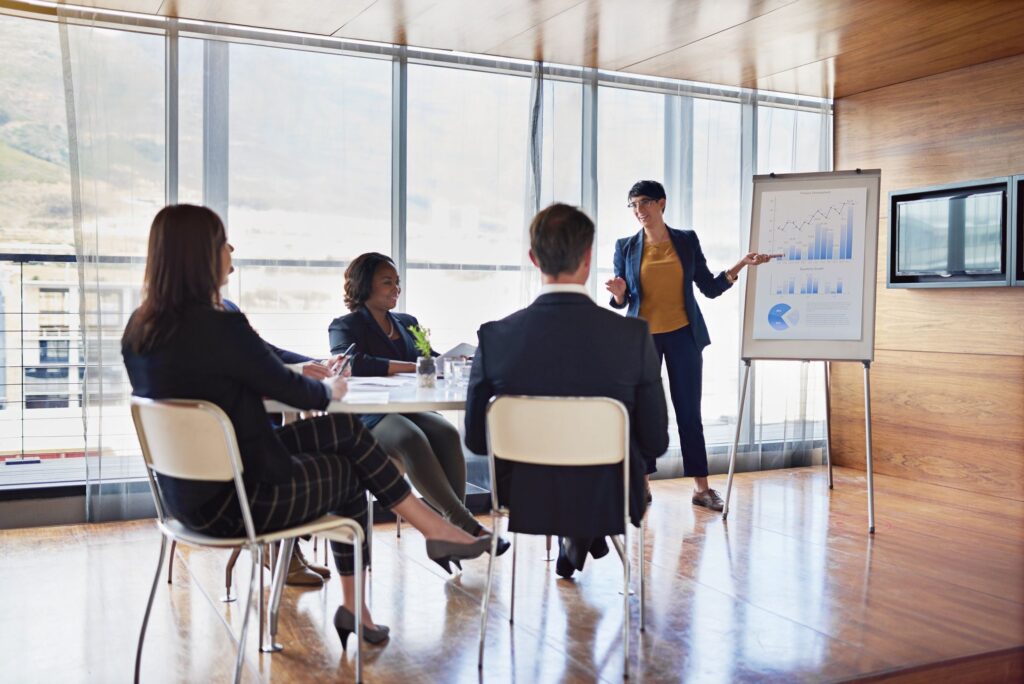 A woman leading a presentation with financial growth charts on an easel board to seated team members.