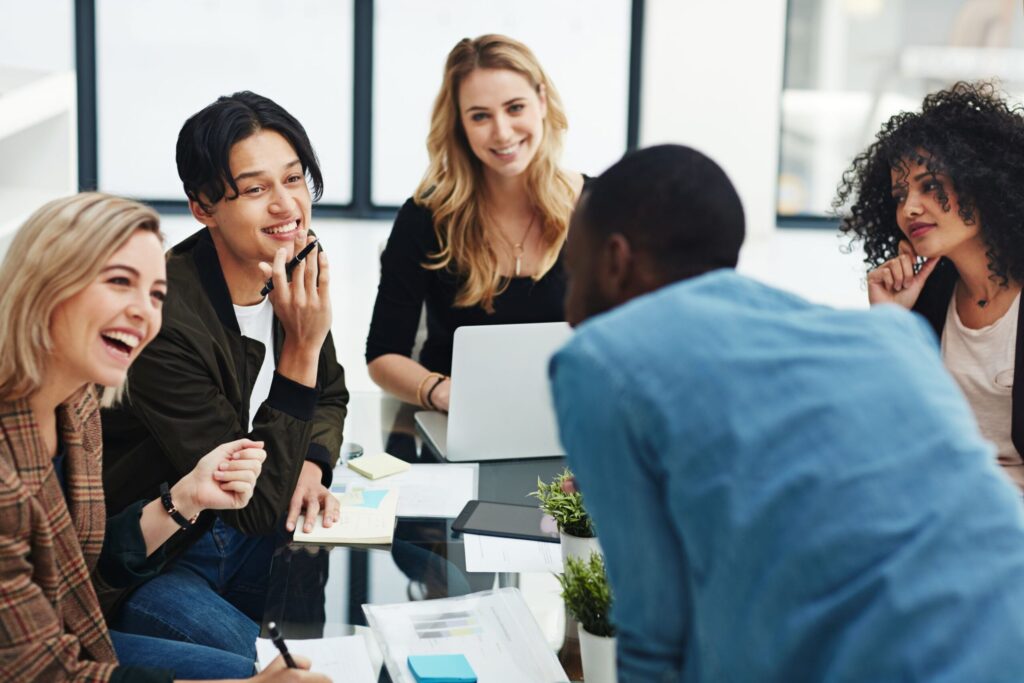 A diverse team of young professionals smiling and collaborating around a glass table during an office meeting.