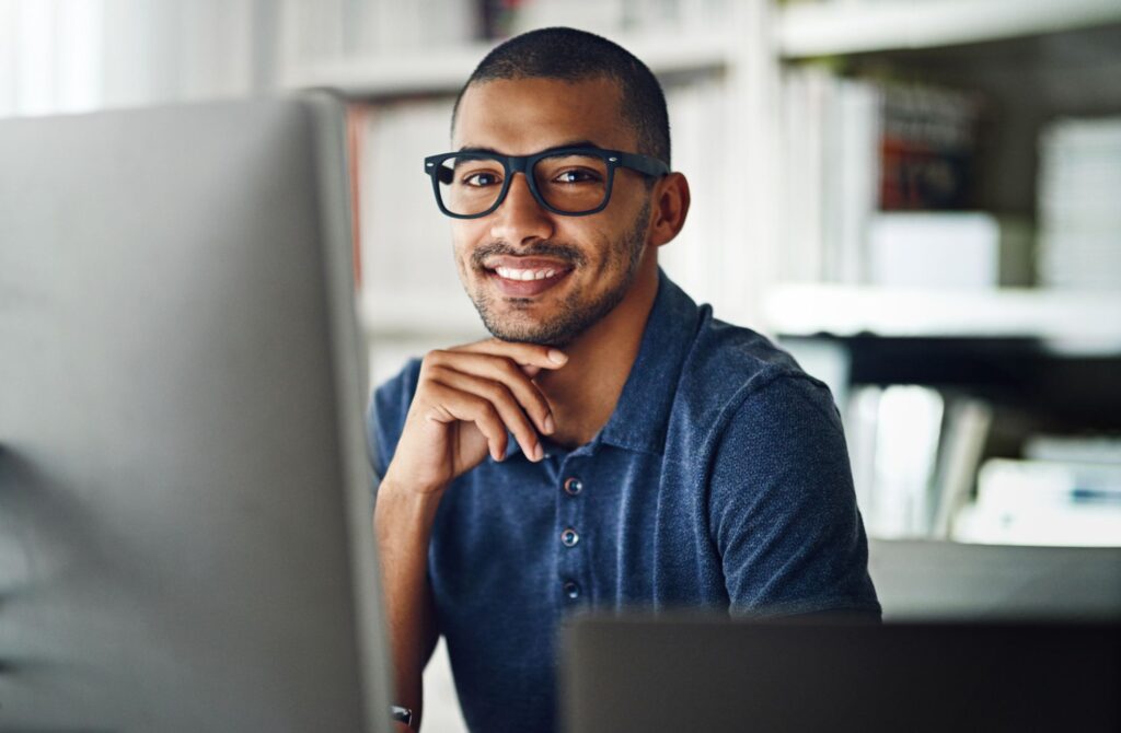 A man in glasses sitting at a computer smiling