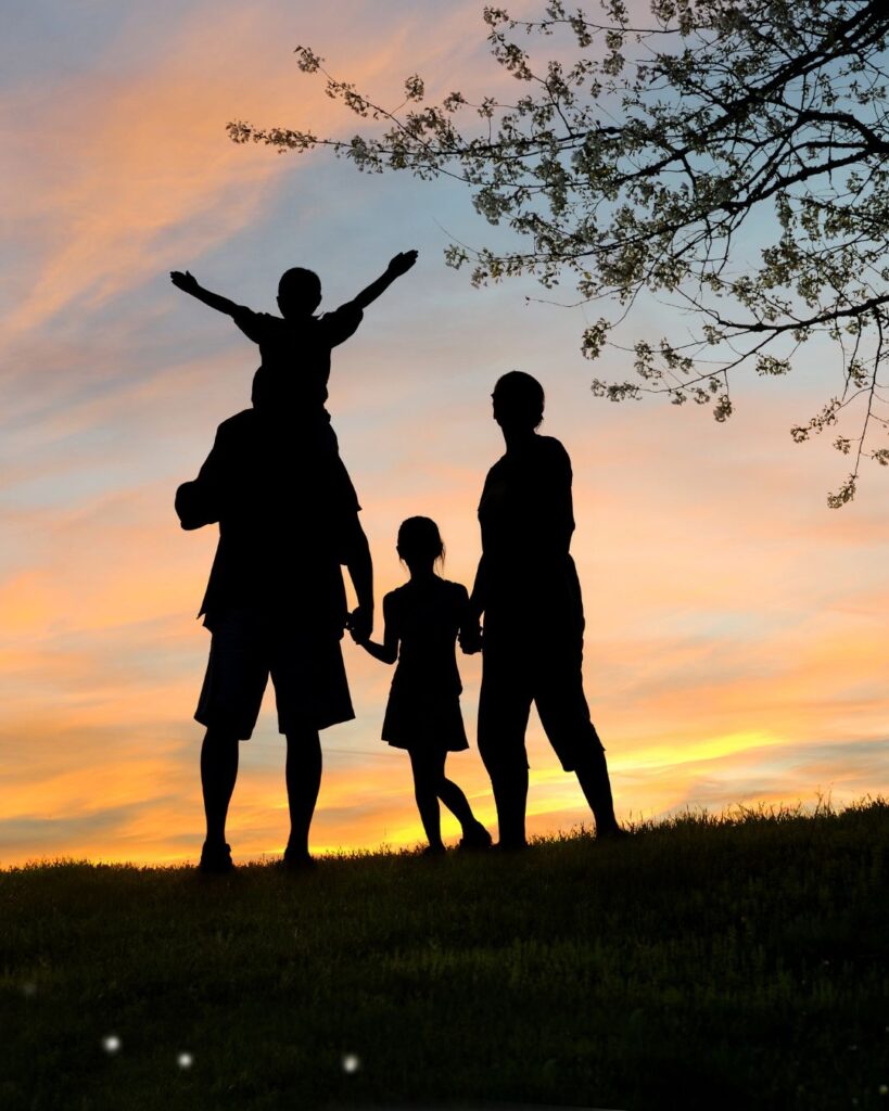 A family of four playing on a grassy hill at sunset
