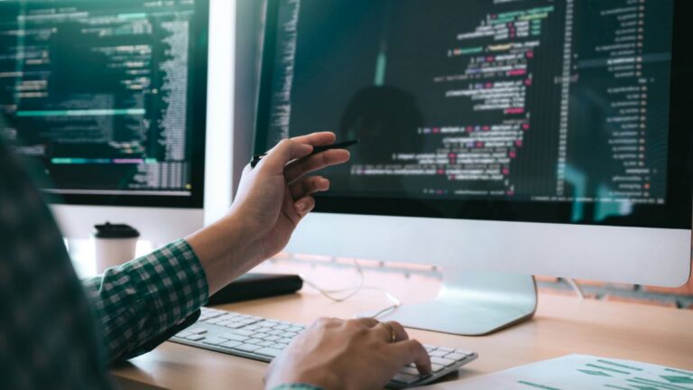 Hand pointing at code displayed on a computer monitor