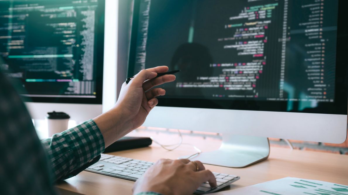 Hand pointing at code displayed on a computer monitor
